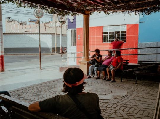 A group of locals relaxing under a shaded area in Pacasmayo, Peru, capturing a typical street scene.