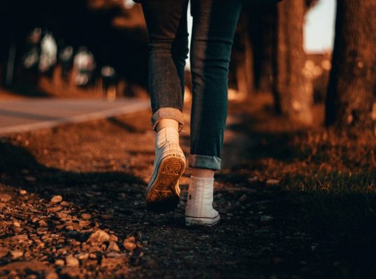 A person in jeans and sneakers walks along a forest path at sunset in Italy.