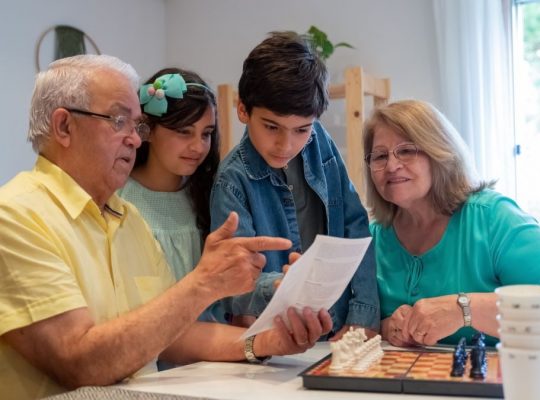 Grandparents teaching grandchildren to play chess in a cozy home setting.