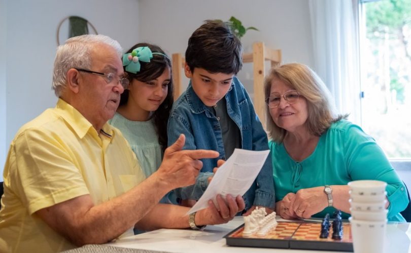 Grandparents teaching grandchildren to play chess in a cozy home setting.