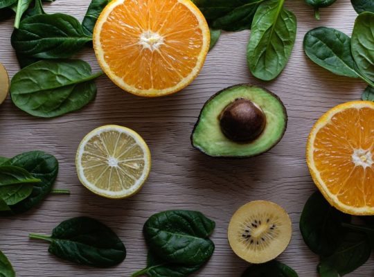 Colorful flat lay of sliced fruits and fresh greens on a wooden table, ideal for healthy lifestyle concepts.