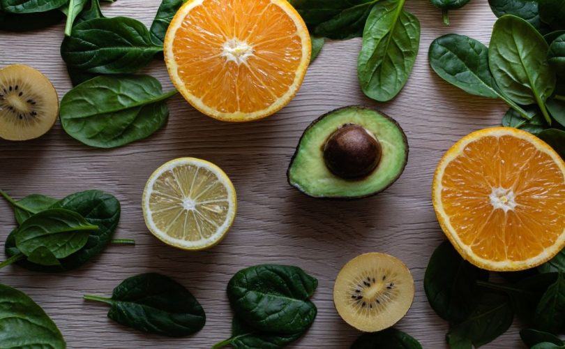 Colorful flat lay of sliced fruits and fresh greens on a wooden table, ideal for healthy lifestyle concepts.